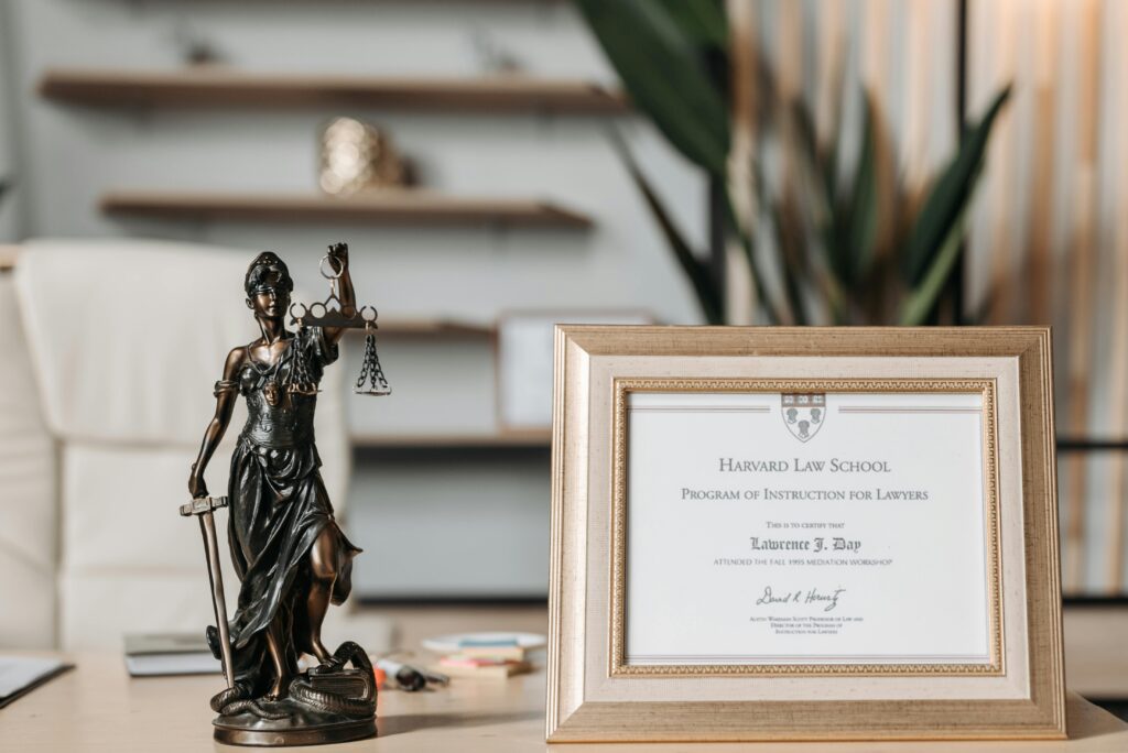 A framed Harvard Law School certificate beside a Lady Justice statue on an office desk.
